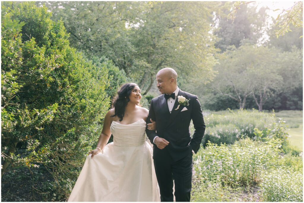 bride and groom surrounded by greenery while smiling at each other